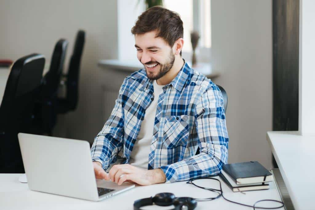 Happy young handsome man wearing casual shirt working on laptop in office and smiling