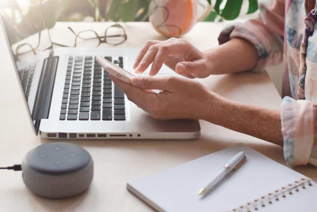 Woman sitting at desk in front of laptop computer using mobile phone